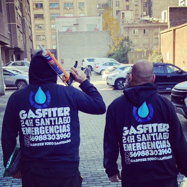 Dos gasfiters del equipo, de espaldas, con polerones de Gasfiter Todo Santiago en una calle de Santiago